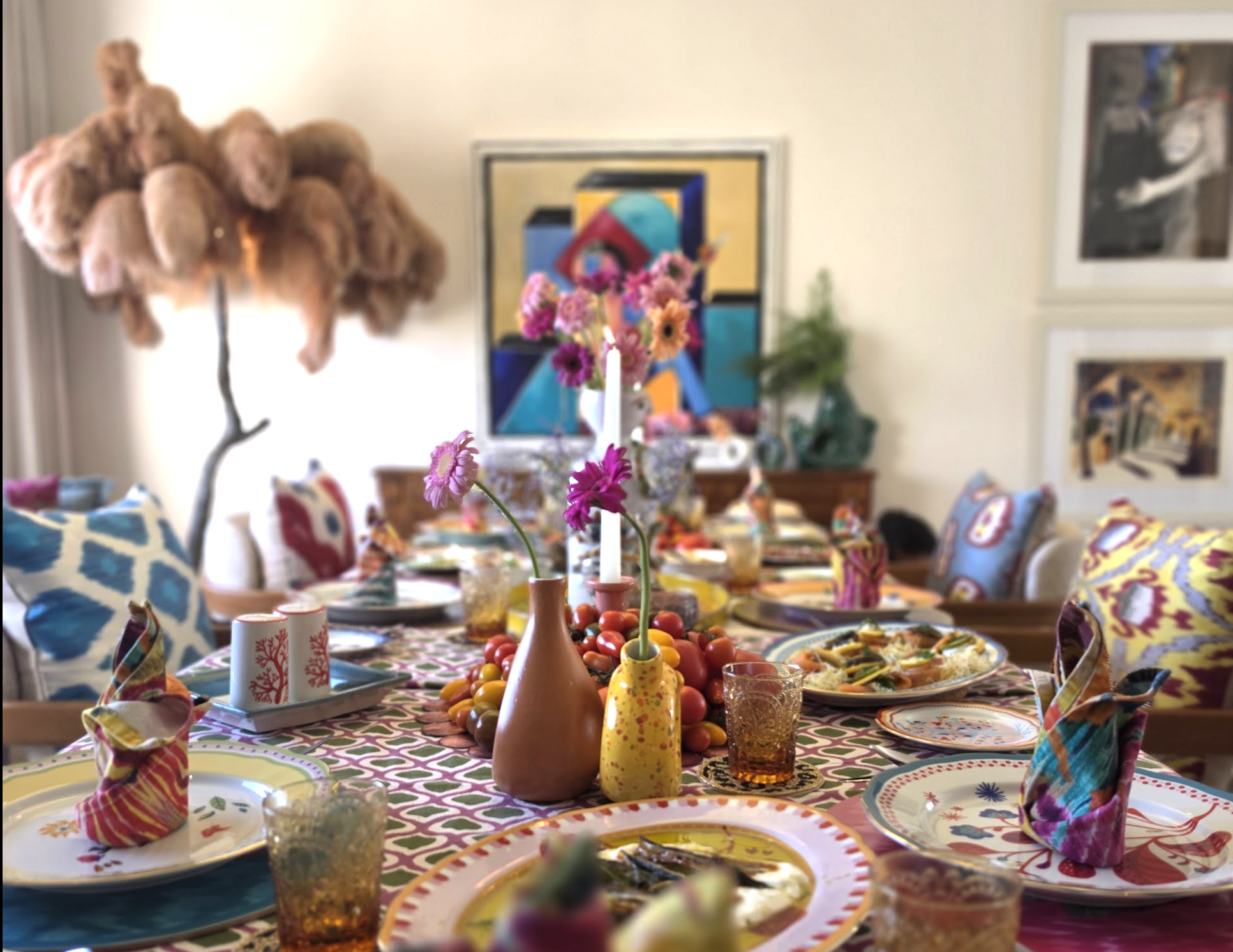 A colorful dining table set with food, flowers, candles and Ové ceramics