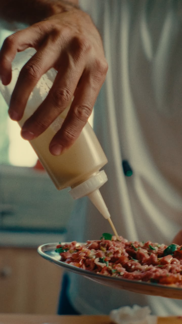 A chef pouring from a white squeeze bottle onto a plated dish